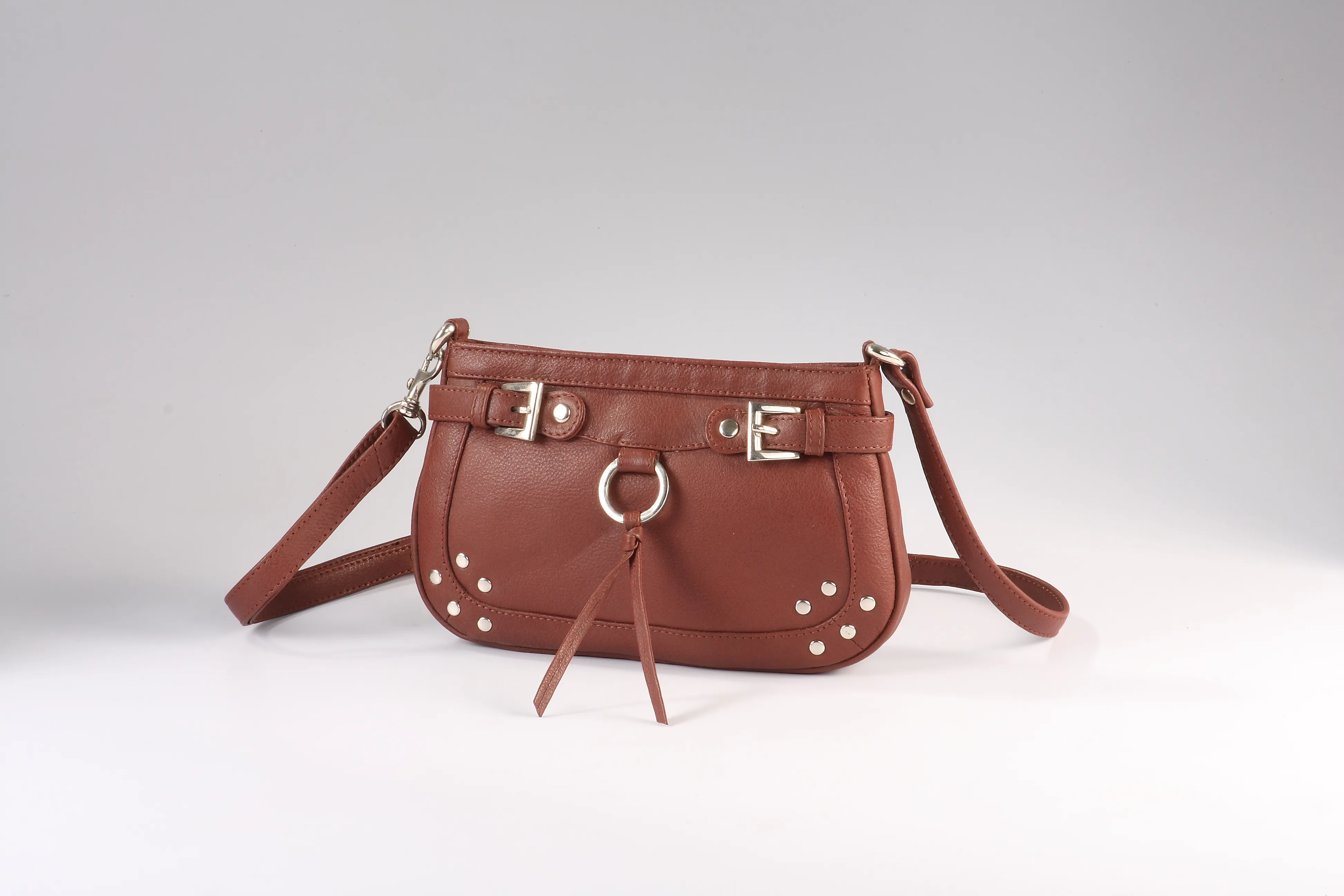 Compact brown leather sling bag with buckle straps, stud accents, and tassel detail.
