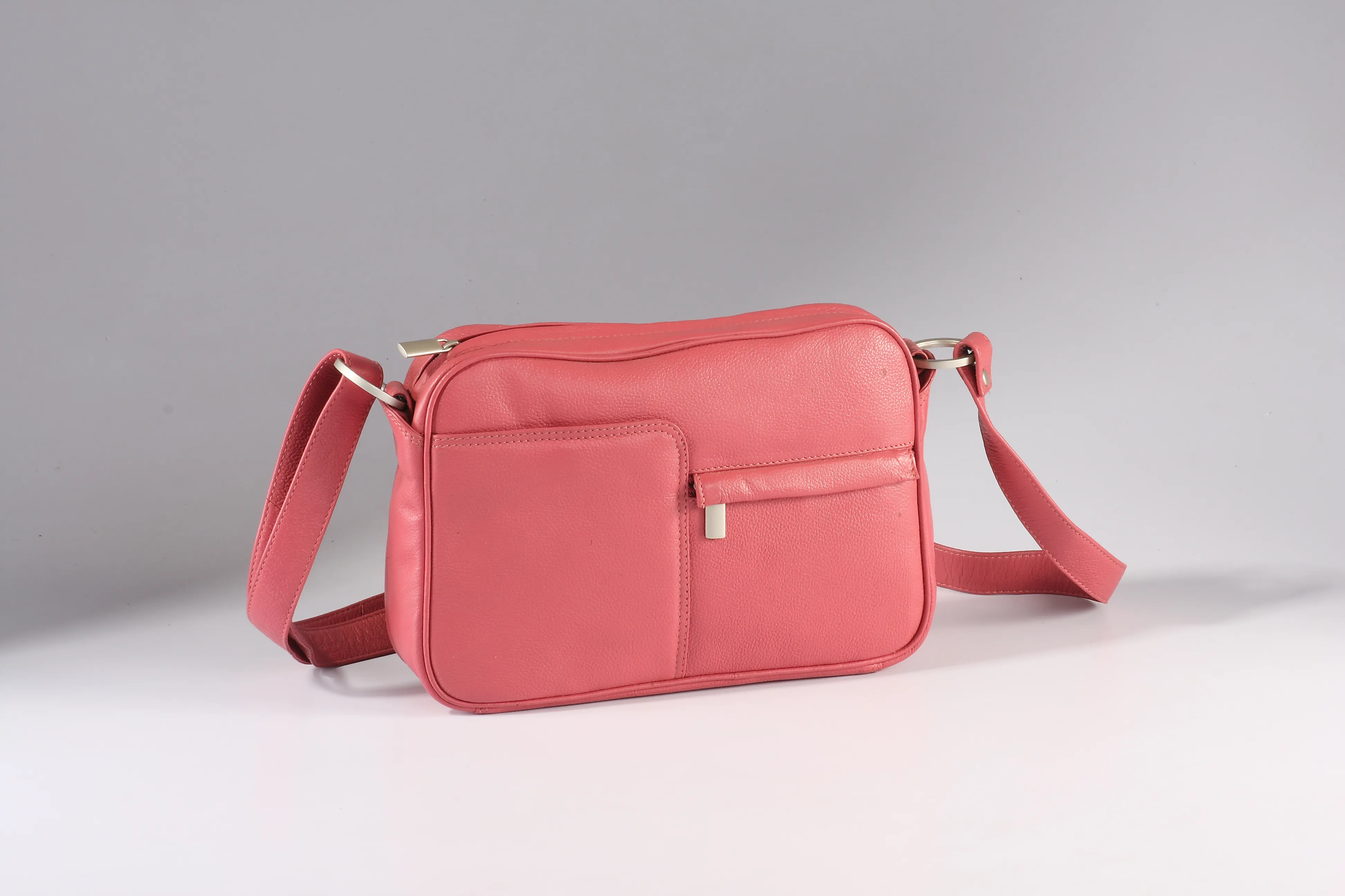 Compact pink leather sling bag with front pockets, back zip, and an adjustable shoulder strap for daily essentials.