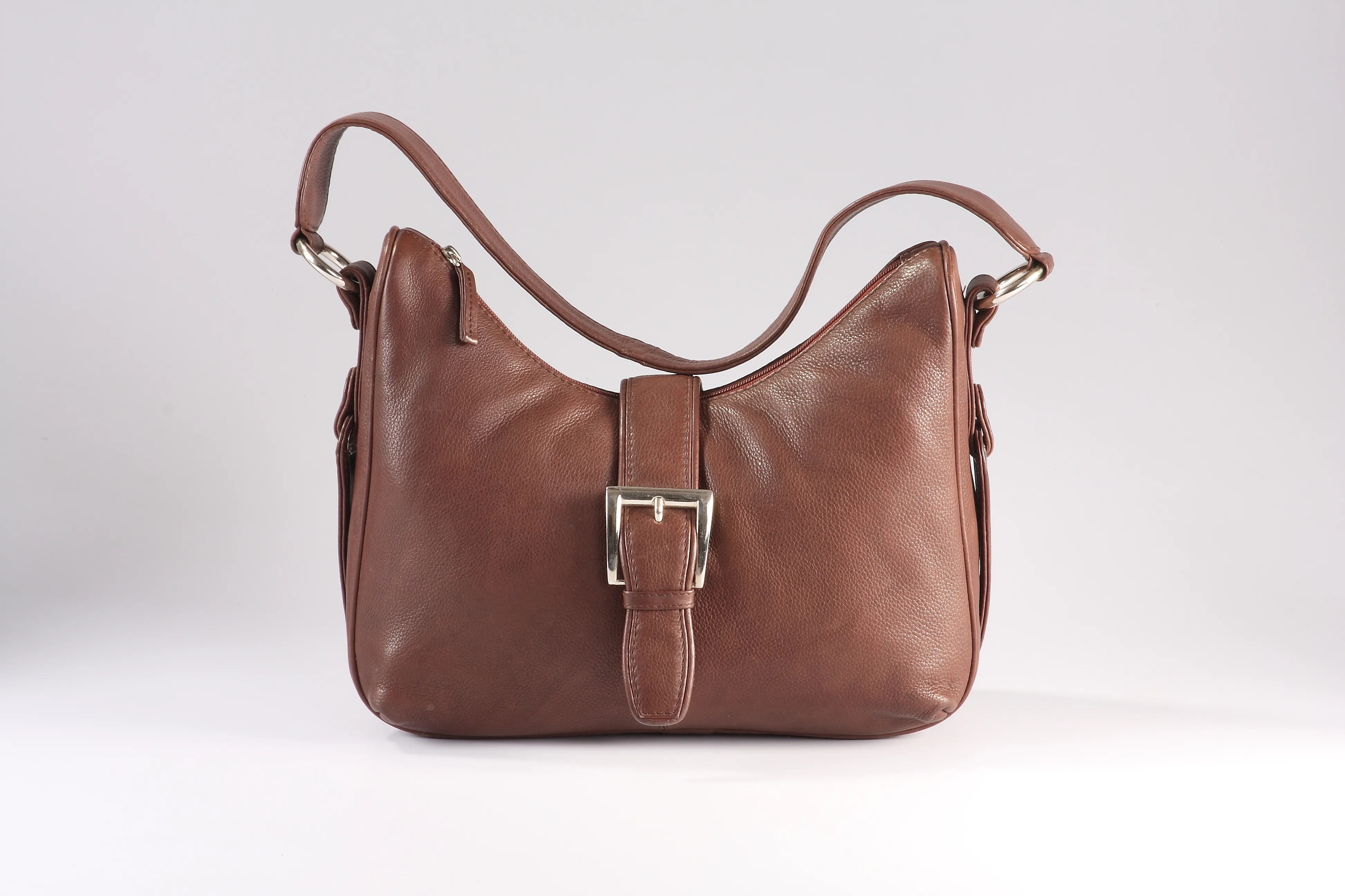 Spacious brown leather hobo bag with crescent top design, brass buckle on flap, and versatile compartments for daily essentials.